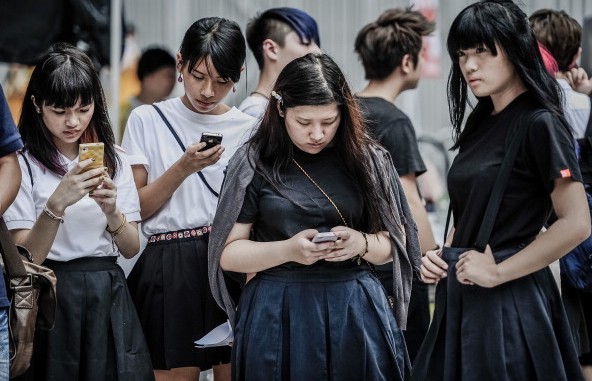 Students check their mobile phones in front of the Central Government Complex in Hong Kong on September 4, 2012 as students and teachers protested for a sixth straight day against plans to introduce Chinese patriotism classes. Protesters at the government headquarters said they would not vote for parties that supported "national education", which they say is a bid to brainwash children with Chinese Communist Party propaganda.     AFP PHOTO / Philippe Lopez        (Photo credit should read PHILIPPE LOPEZ/AFP/GettyImages)
